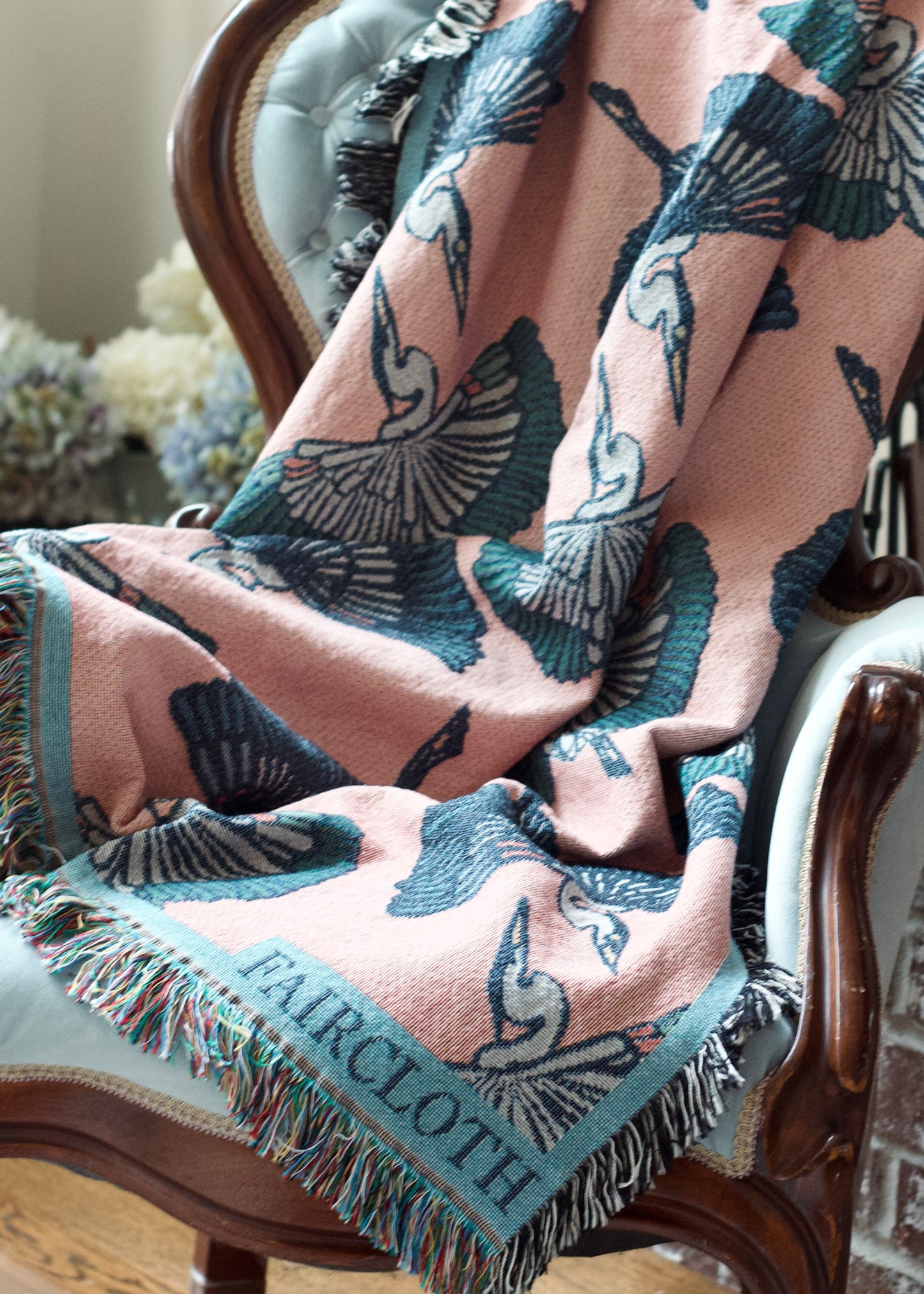 pink faircloth blanket with tiled blue and green herons on a chair