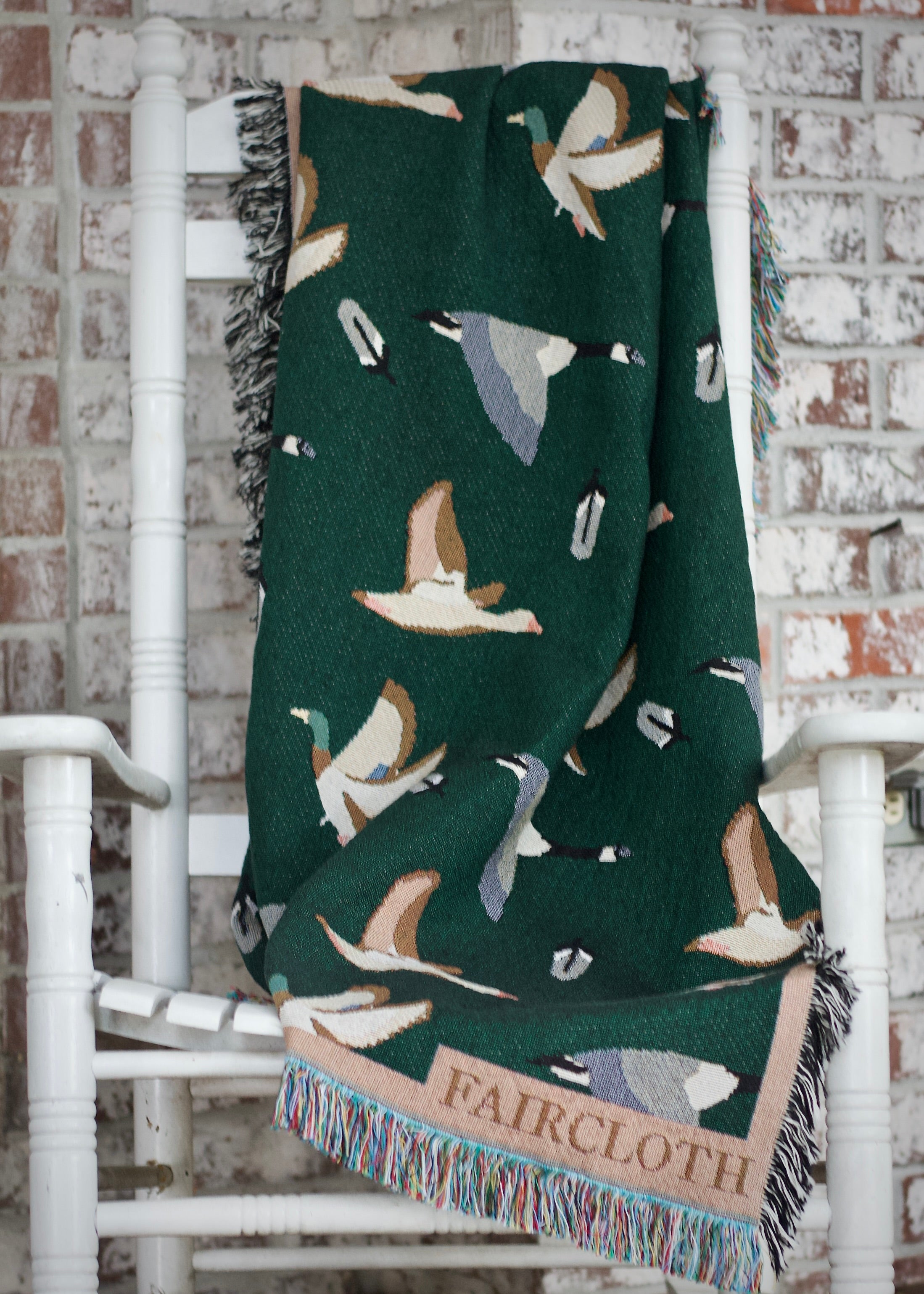 Green blanket with bird pattern draped over a white chair against a brick wall.