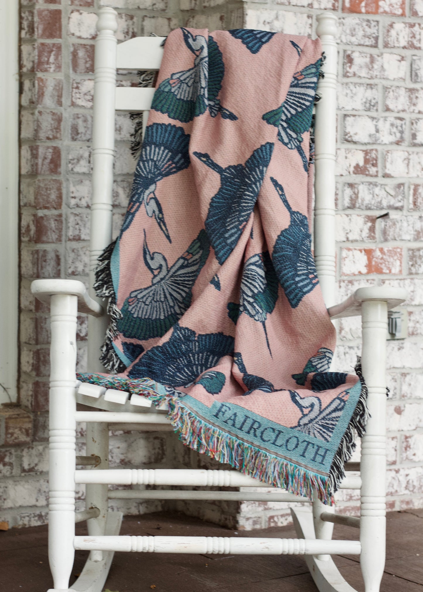 pink faircloth blanket with tiled green and blue herons on a white rocking chair